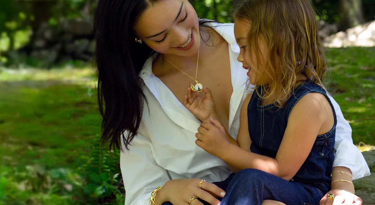 mother and daughter at a park, daughter holding the mothers necklace while sitting on her lap
